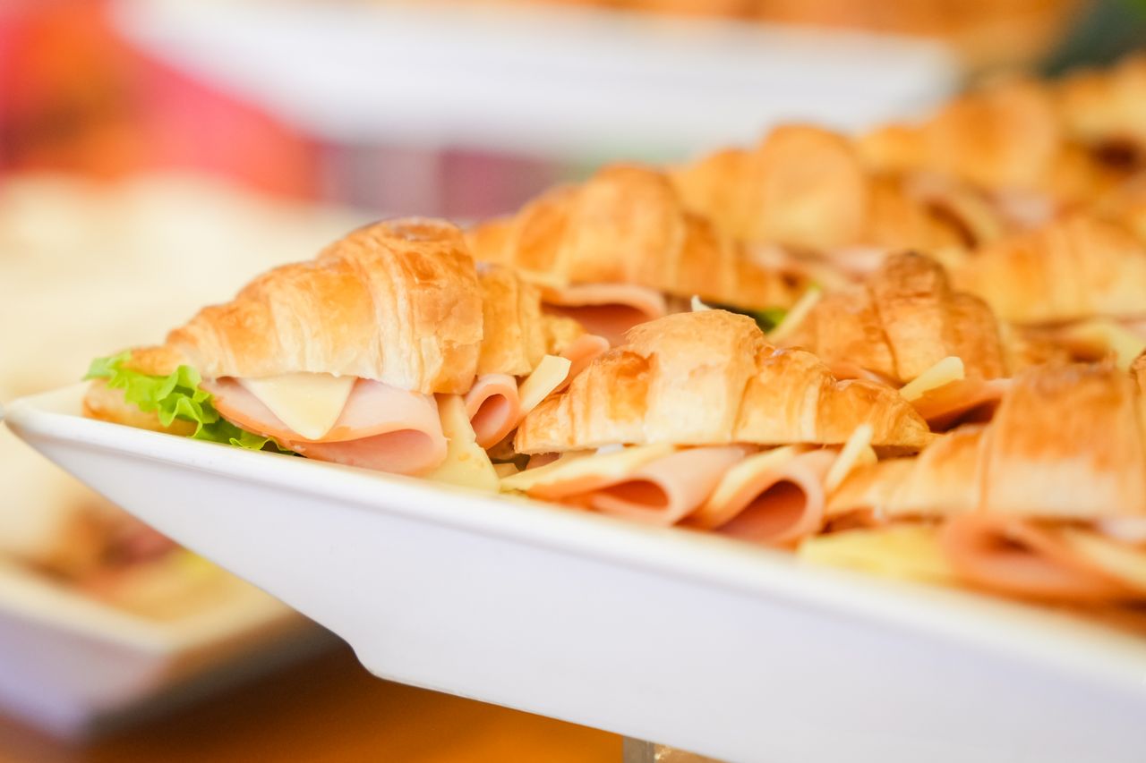 Close-up view of fresh croissant sandwiches with ham, cheese, and lettuce on a white plate.